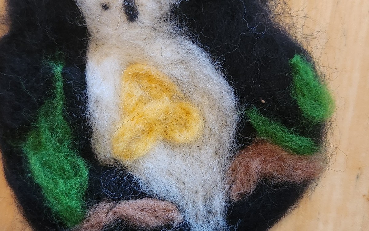 Needle-felted white mouse resting in a dark felt nest